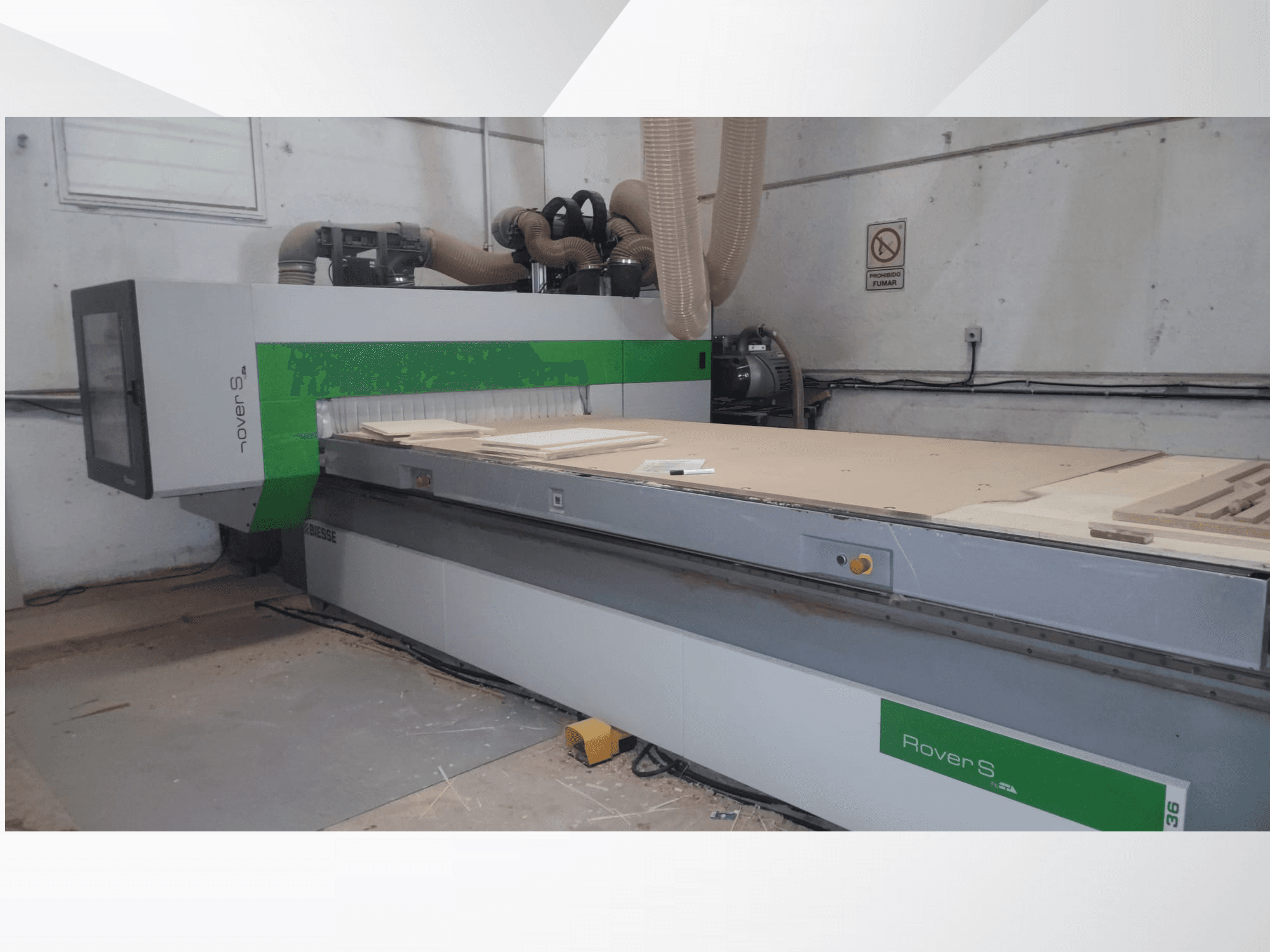 Pohled zepředu na CNC stroj Biesse Rover S s velkou pracovní plochou s dřevěnými panely a hadicemi pro odsávání prachu.