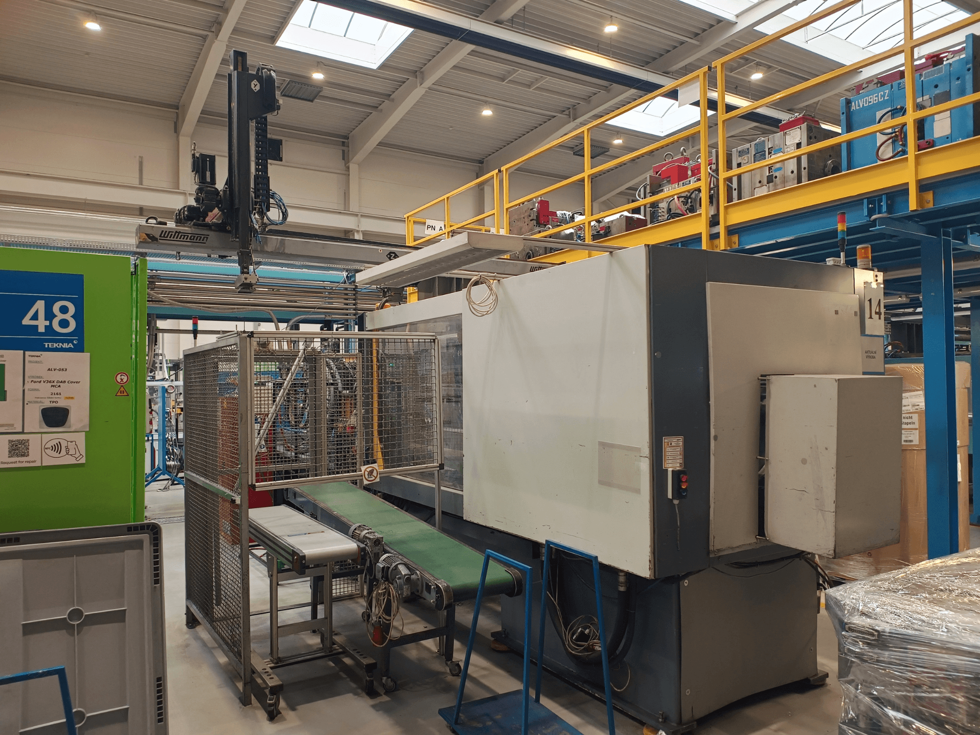 Průmyslový automat od společnosti Winmon, boční pohled zobrazující dopravní pás, ovládací panel a bezpečnostní klec v továrním prostředí.