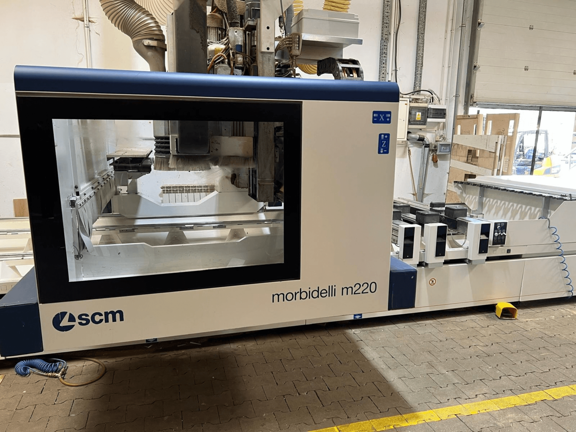 Pohled zepředu na CNC obráběcí centrum SCM Morbidelli M220, na kterém je vidět velké okno, ovládací panel a pracovní prostor.