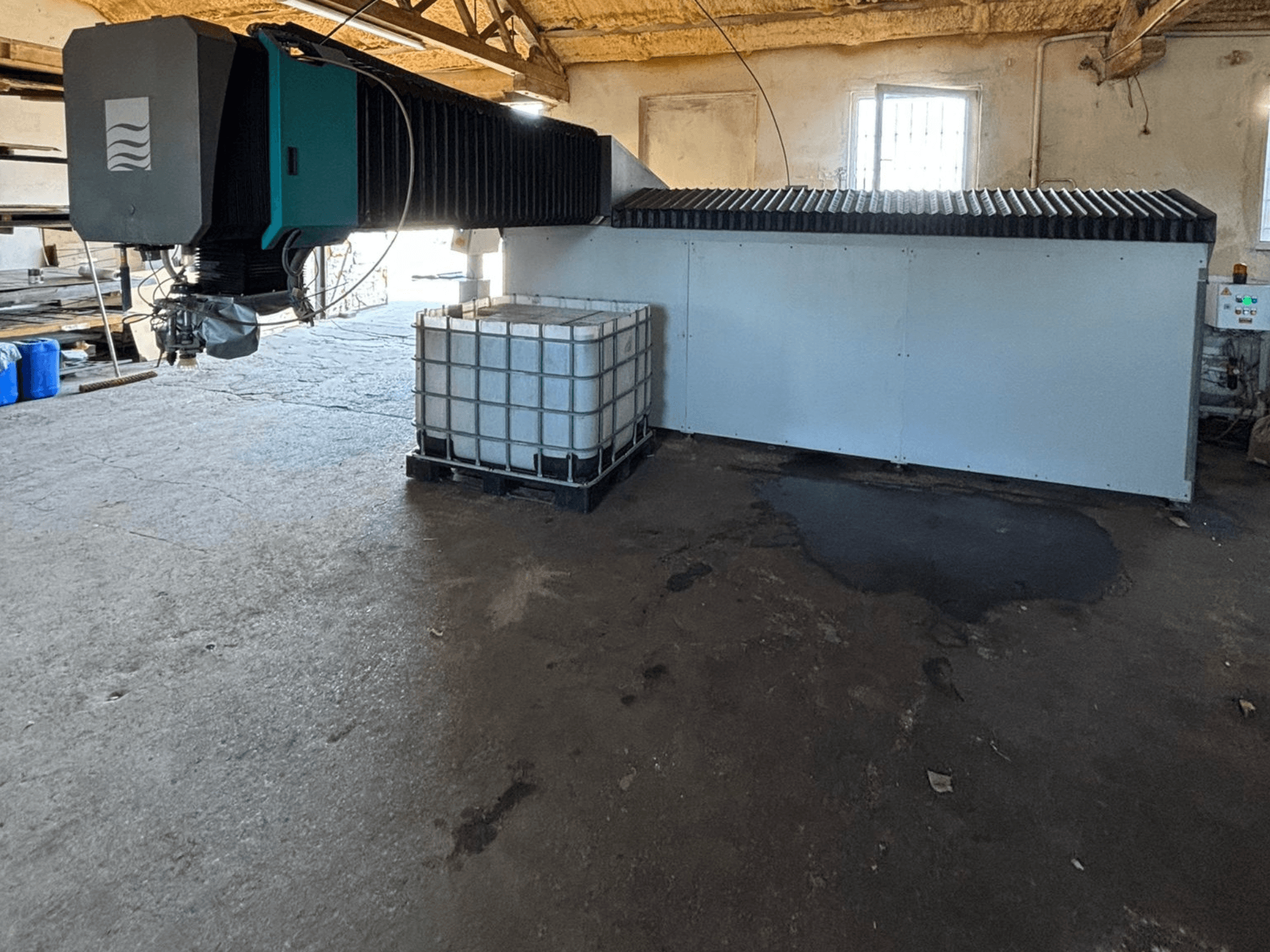 Průmyslový vodní paprsek v dílně, pohled z boku, vedle něj je vidět velká nádrž na vodu a ovládací panel.