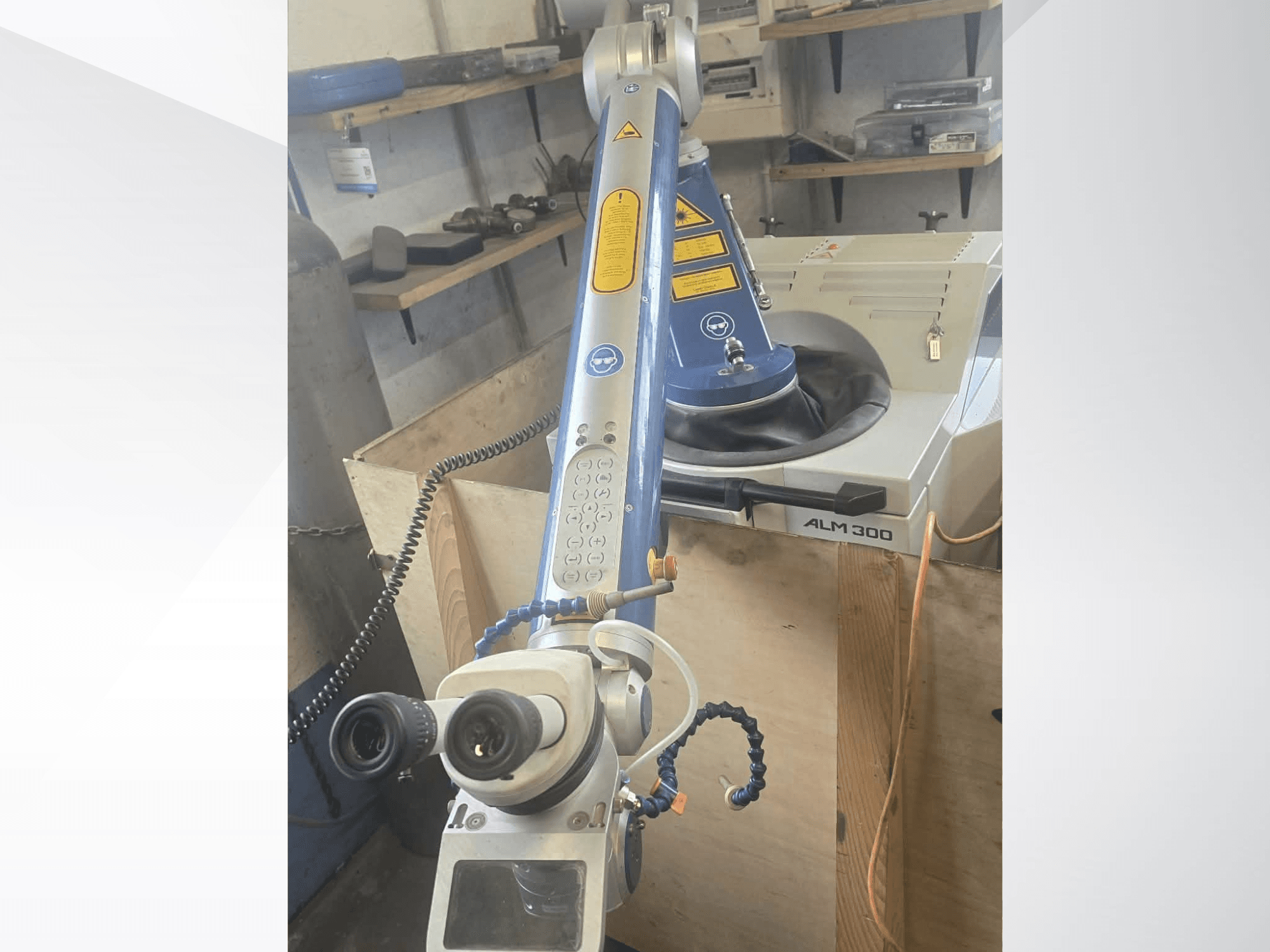 Pohled zepředu na laserový svařovací stroj ALPHA LASER ALM 300 s robotickým ramenem, optickými čočkami a ovládacím panelem.
