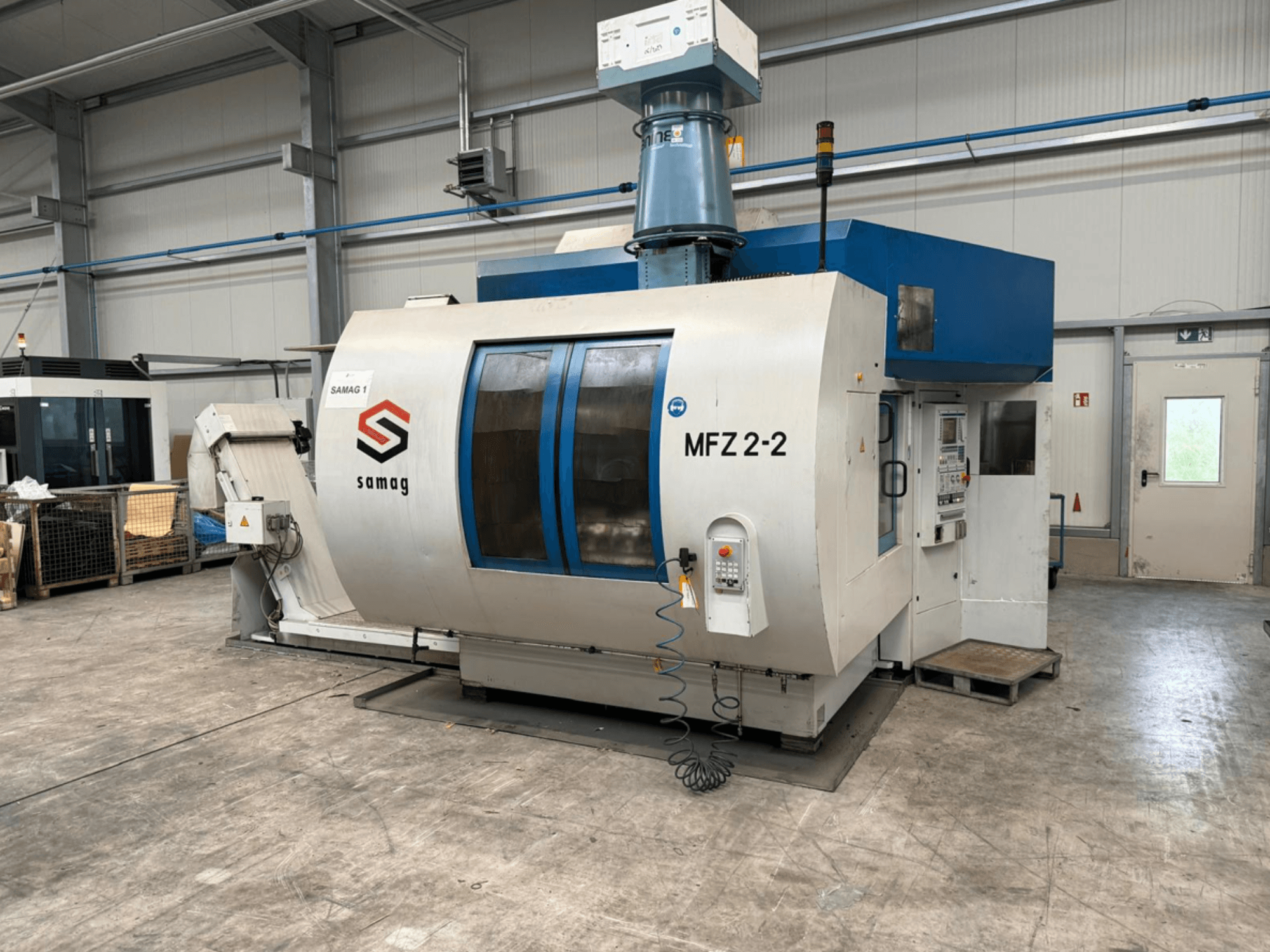 Obráběcí stroj Samag MFZ 2-2, pohled zepředu, zobrazující ovládací panel a modrou horní část, s bezpečnostními prvky v průmyslovém prostředí.