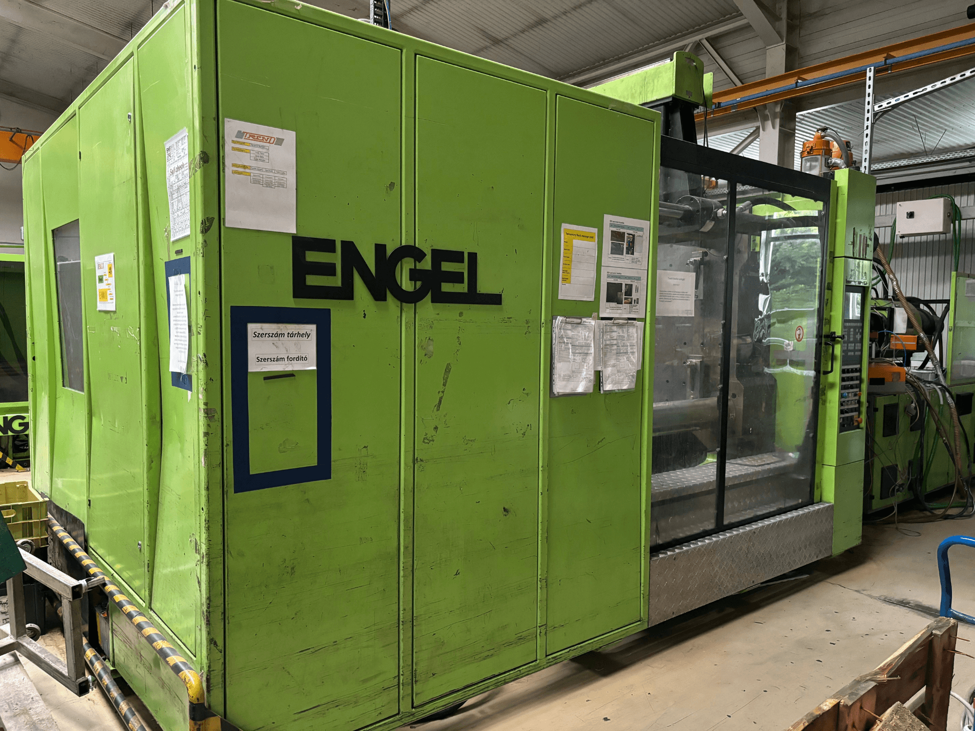 Hydraulický vstřikovací stroj Engel DUO 5550/800, pohled zepředu, se zeleným vnějším povrchem a průhledným přístupovým panelem.