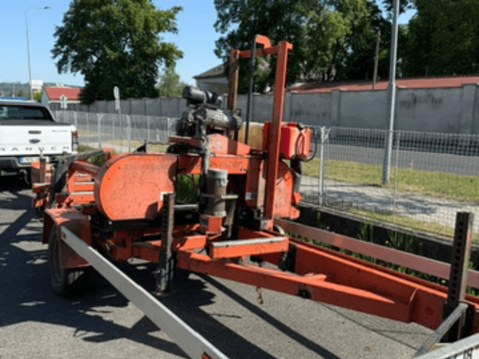 Pásová pila na dřevo WOOD-MIZER LT40 v oranžové barvě, boční pohled na přívěsu s viditelnými koly a součástmi motoru.