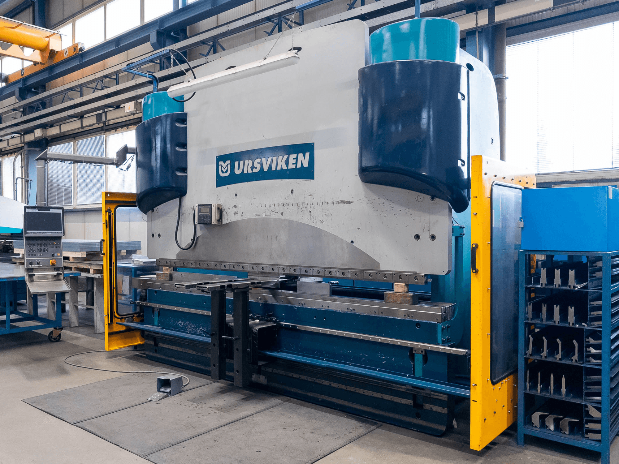 Lisovací stroj Ursviken Optiflex 130 3.1M ve výrobním prostředí, pohled zepředu a ovládací panel.