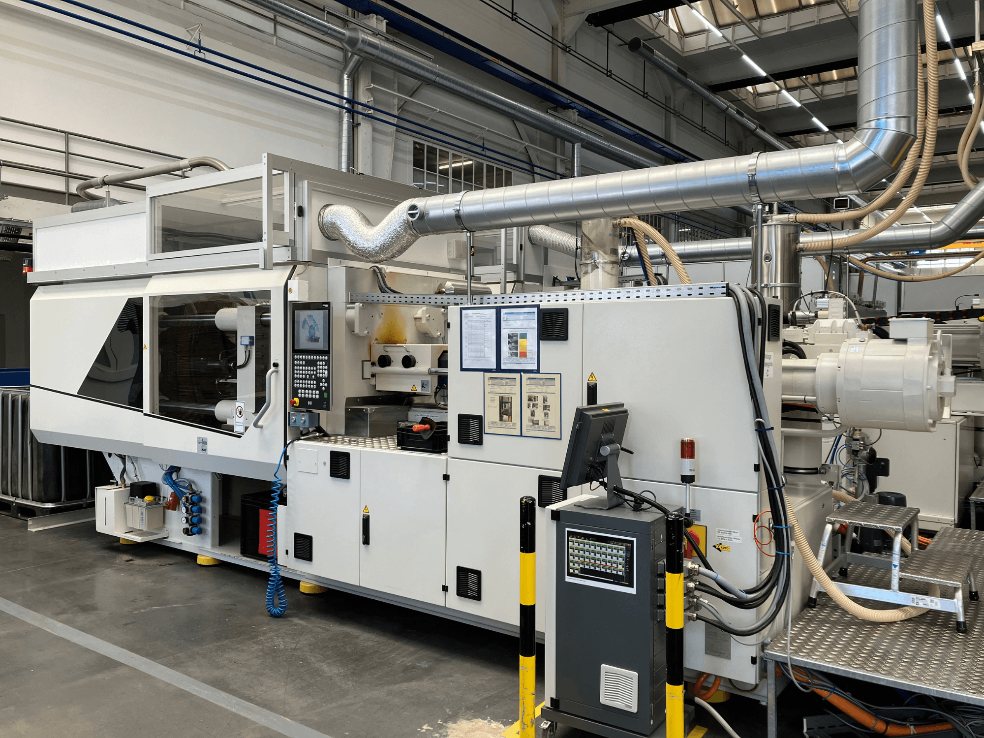 Pohled zepředu na průmyslový stroj s ovládacím panelem, potrubím a obrazovkami displeje s elegantním bílým designem a technickými detaily.