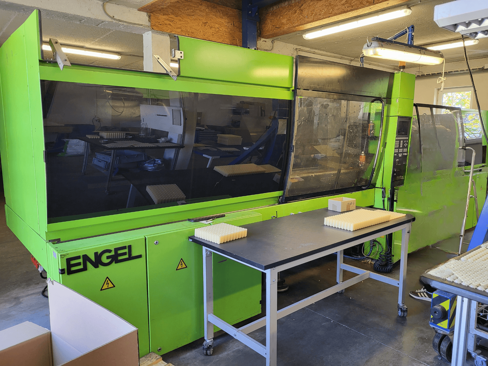 Hydraulický vstřikovací stroj Green Engel ES1800/300HL při pohledu zepředu, s naskládanými materiály na pracovním stole.
