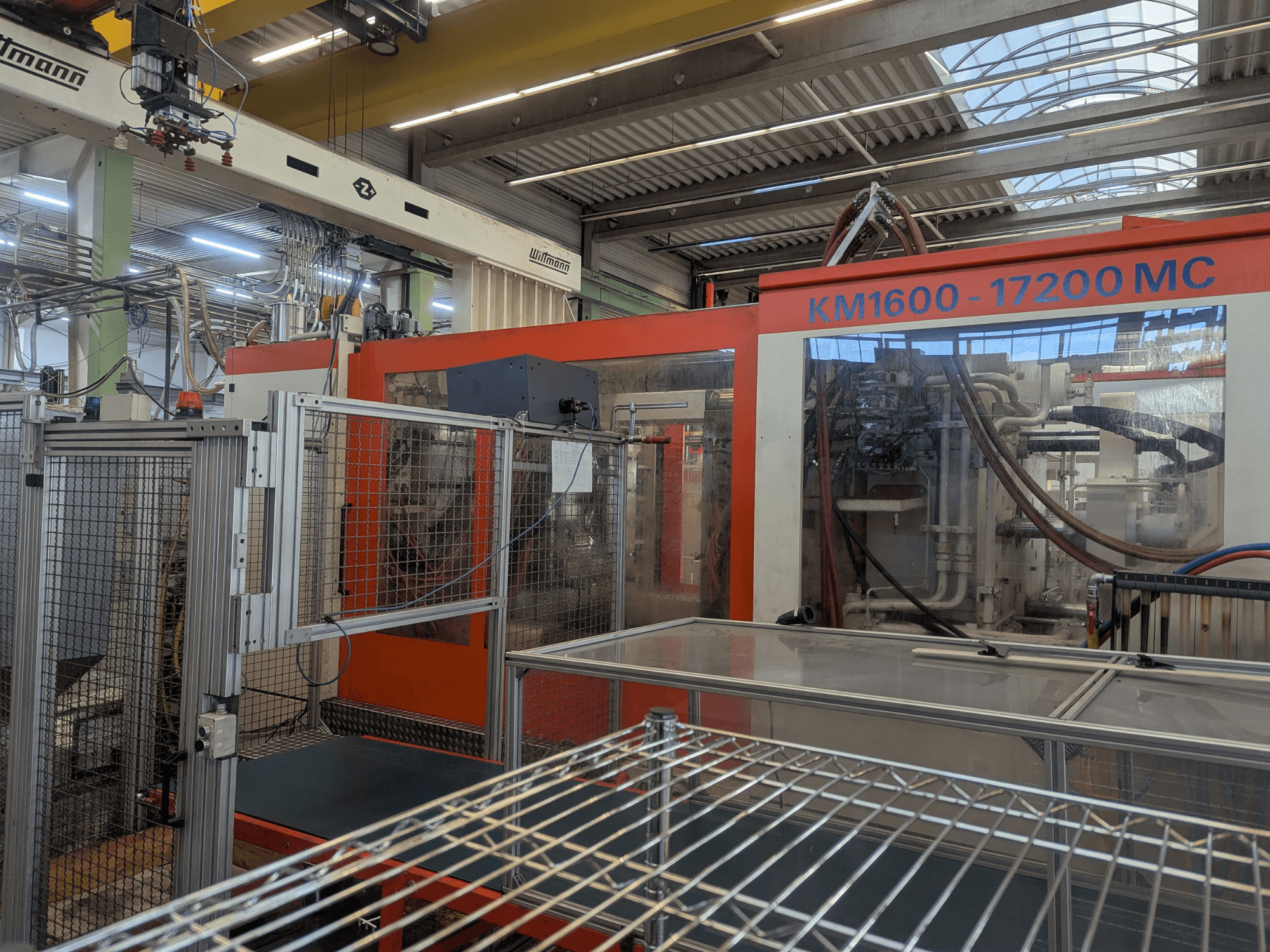 Hydraulický vstřikovací stroj Krauss Maffei KM 1600-17200MC, pohled zepředu s viditelným ovládacím panelem a hydraulickým vedením.