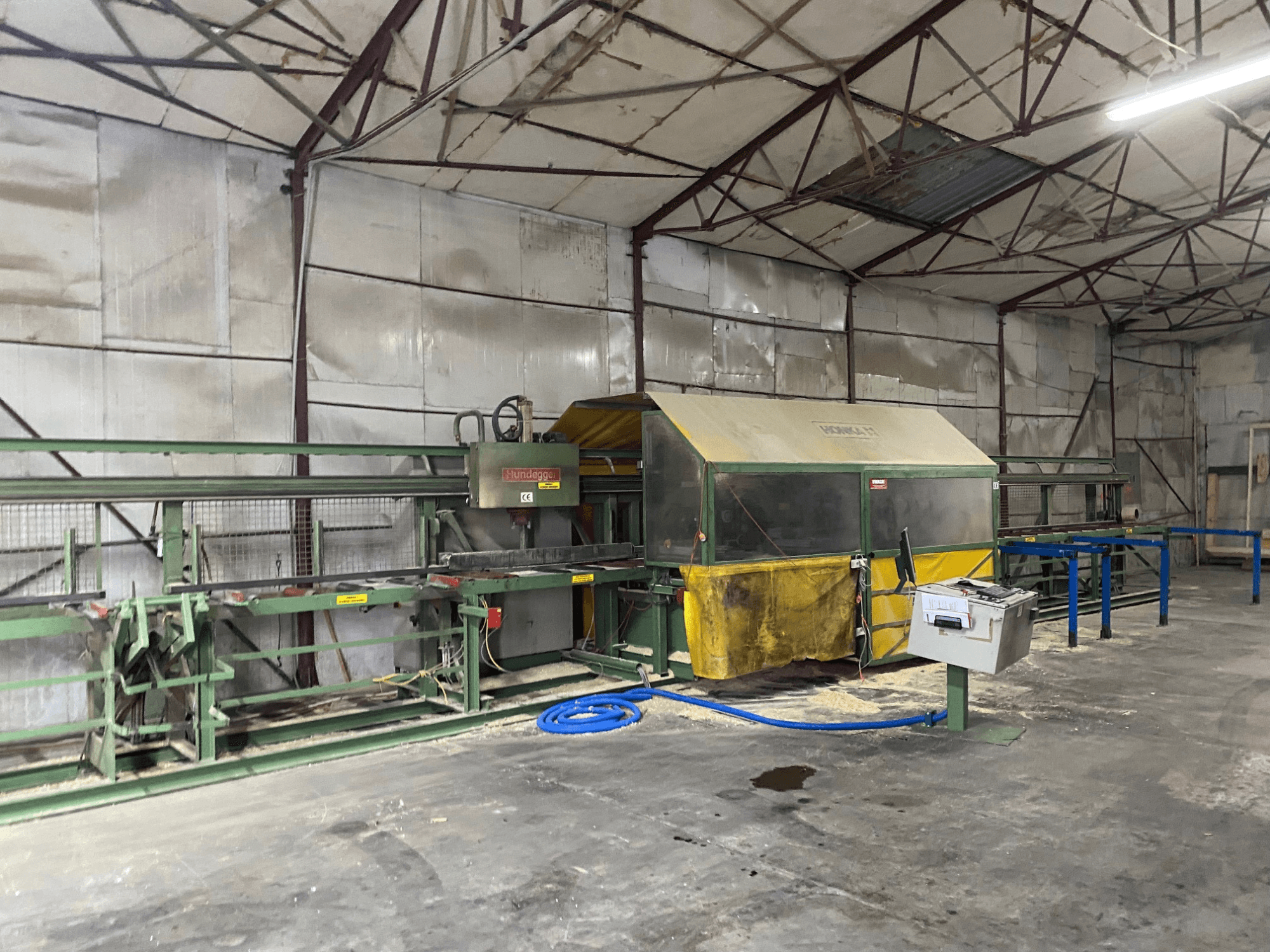 CNC dřevoobráběcí centrum HUNDEGGER K1 v dílně, boční pohled na stroje, ovládací prvky a piliny na podlaze.