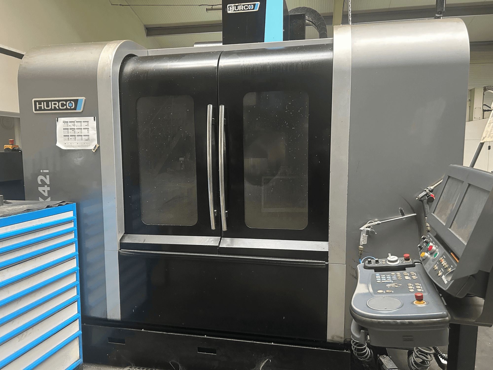 Stroj Hurco VMX42i CNC, pohled zepředu s ovládacím panelem na boku, s dvojitými dveřmi a viditelnými technickými detaily.