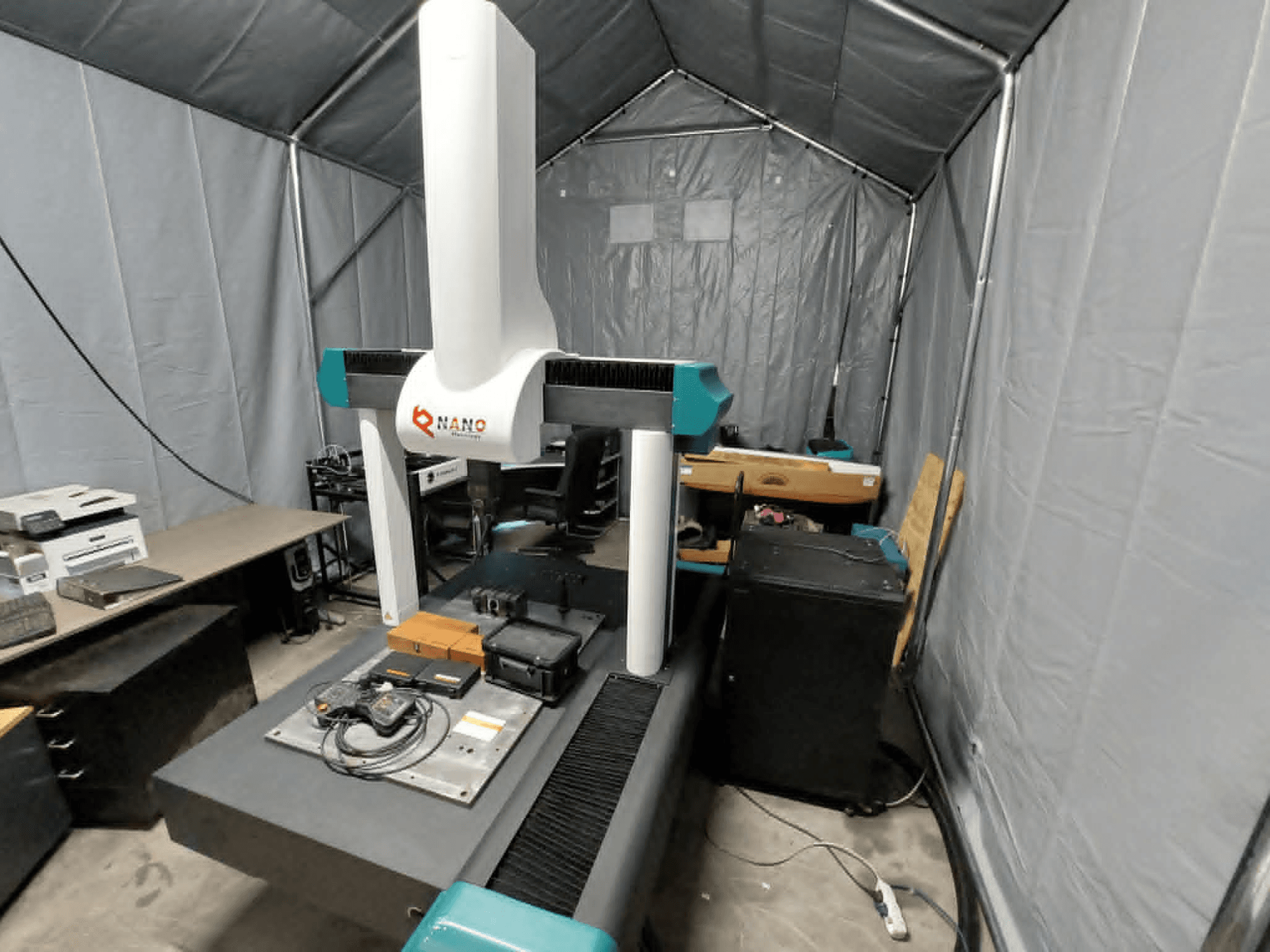 Souřadnicový měřicí stroj NANO METROLOGY Micr 7106 ve stanu; čelní pohled ukazuje rameno stroje a měřicí plošinu s příslušenstvím.