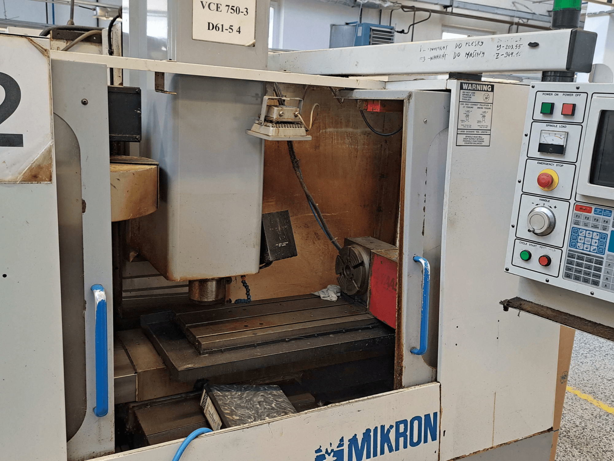 Pohled zepředu na frézku Mikron VCE 750-3, zobrazující vřeteno, ovládací panel a pracovní stůl s technickými detaily.