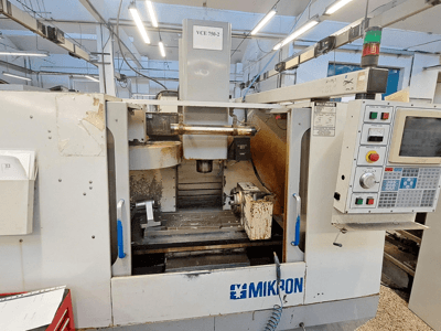 CNC frézka Mikron VCE 750-2, pohled zepředu, s ovládacím panelem a vřetenem v obráběcím prostoru, jeví známky opotřebení a špíny.
