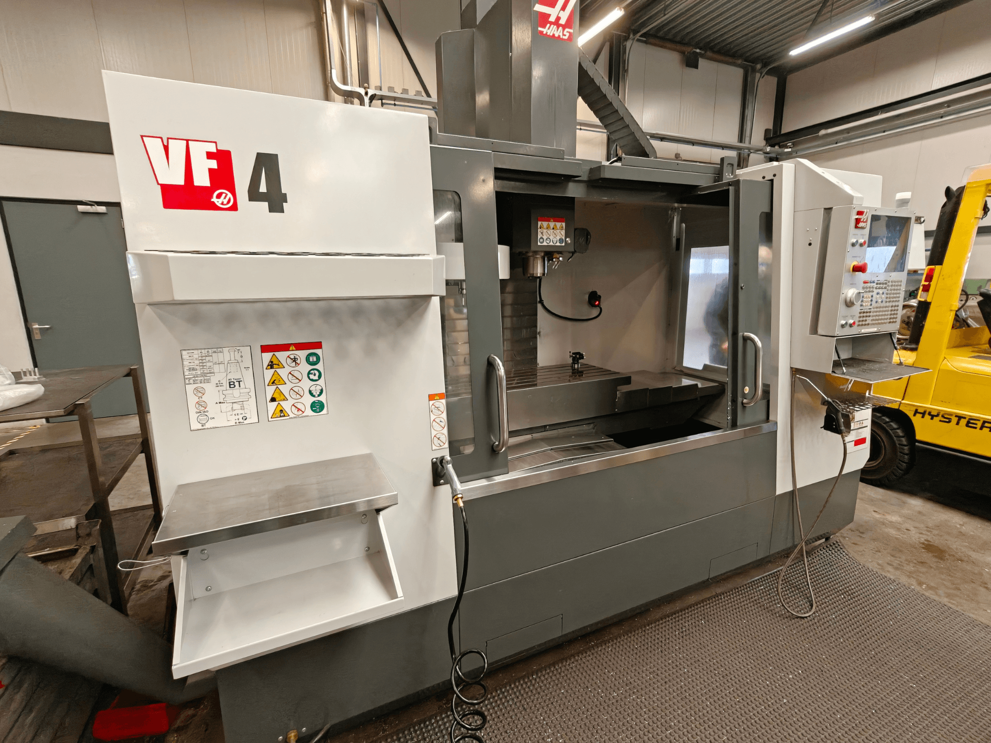 Vertikální obráběcí centrum HAAS VF-4, pohled zepředu, s ovládacím panelem, pracovním prostorem a bezpečnostními štítky na boku.