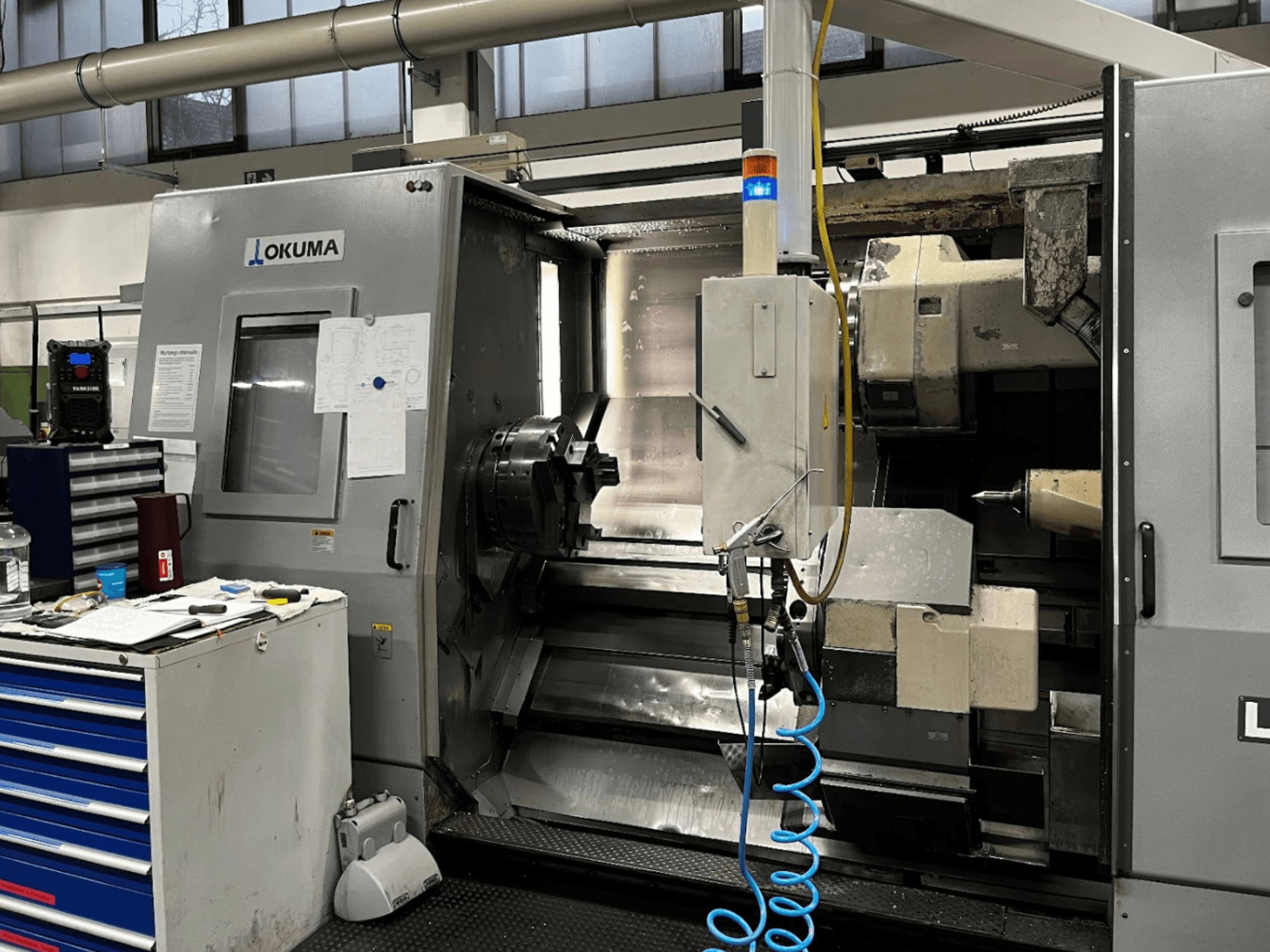 Horizontální soustruh Okuma LU35-M, pohled zepředu. Ovládací panel, nástroje a velké sklíčidlo pro obrábění.