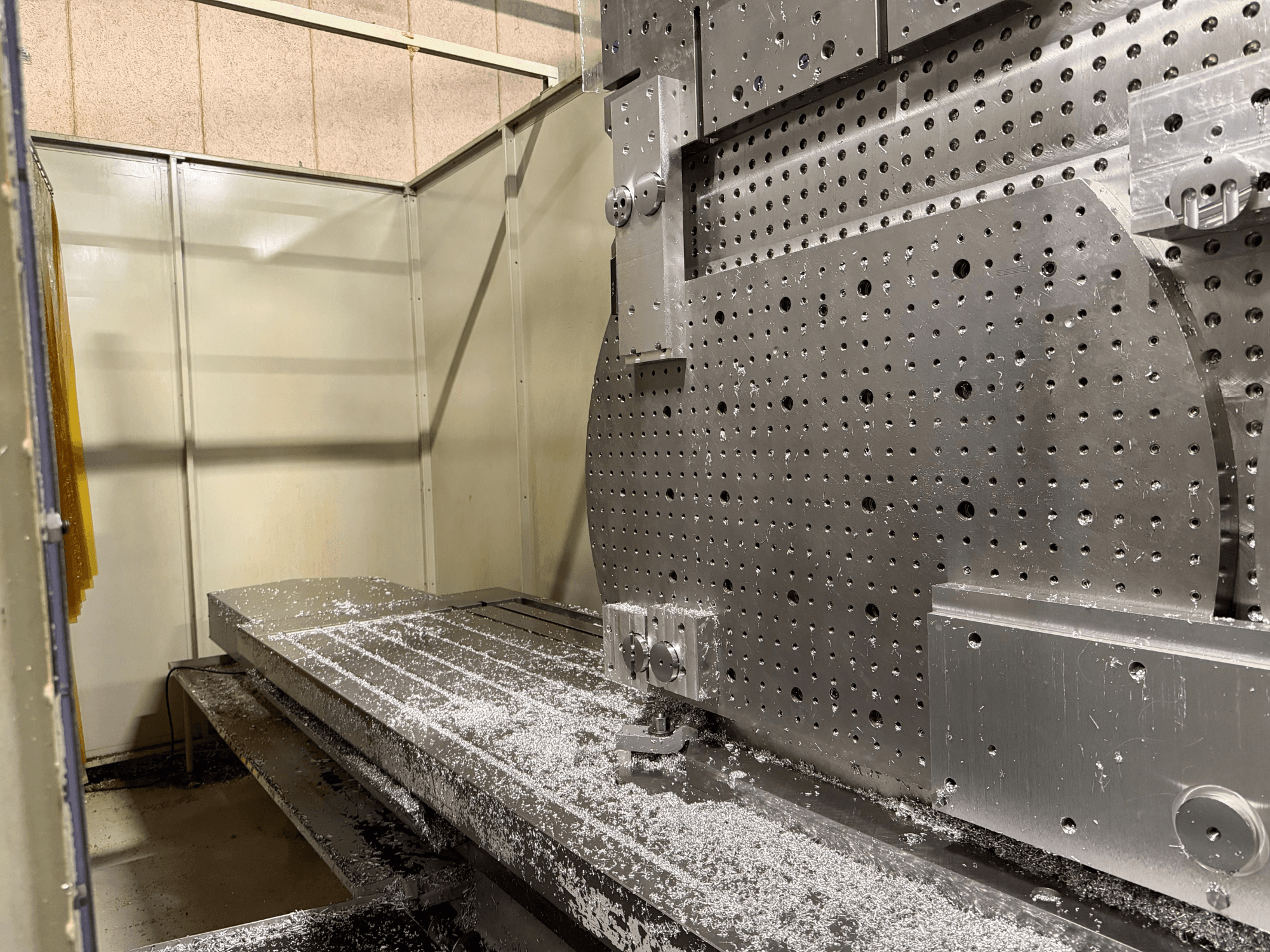 Pohled zepředu zblízka na univerzální obráběcí centrum KIHEUNG KNC-U1000, na kterém je vidět kovový pracovní stůl s hliníkovými hoblinami.